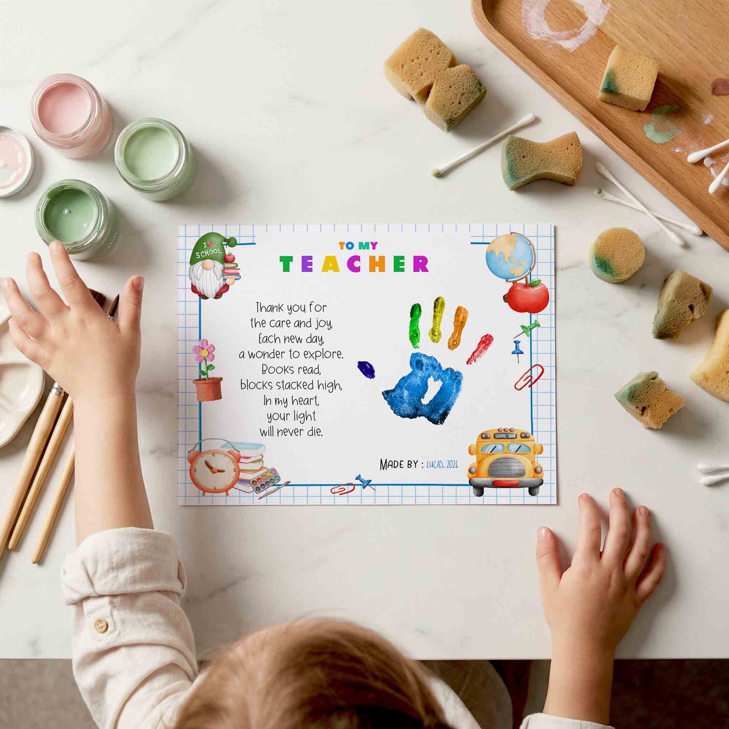 Child's hands reaching towards a card with 'To My Teacher' message on a table with art supplies.
