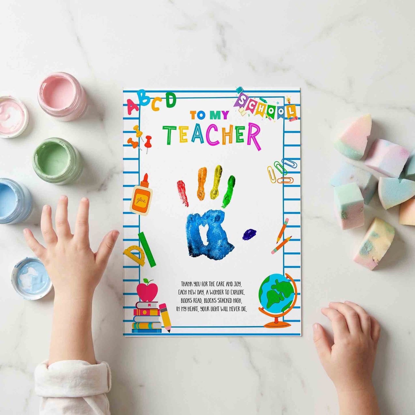 Colorful 'To My Teacher' card with child's handprints and crayon art on a white surface with art supplies.