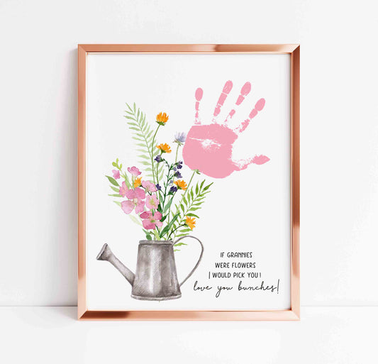 Framed artwork with a pink handprint, flowers, and a watering can on a white background.