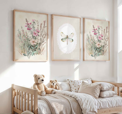 Three framed nursery prints above a toddler bed: two show soft pink wildflowers, and the center piece features a green dragonfly inside an oval lace border.