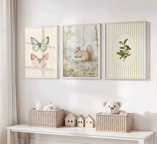 Three framed artworks on a wall above a white shelf with decorative items.