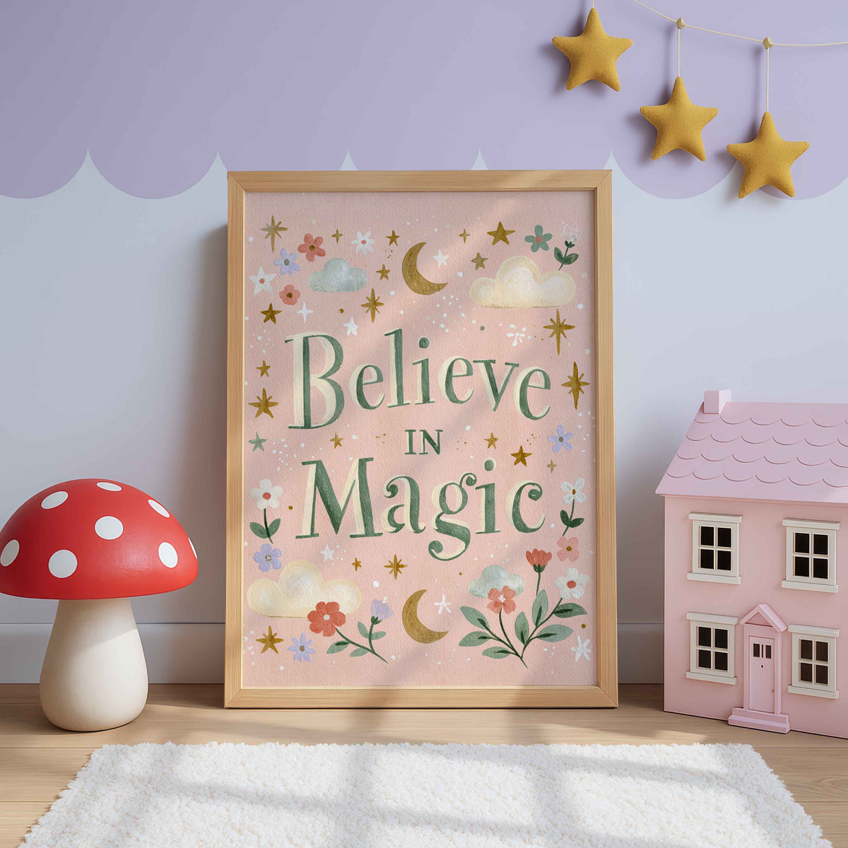Retro wall art with green Believe In Magic lettering on rosy pink, circled by moons, stars and clouds